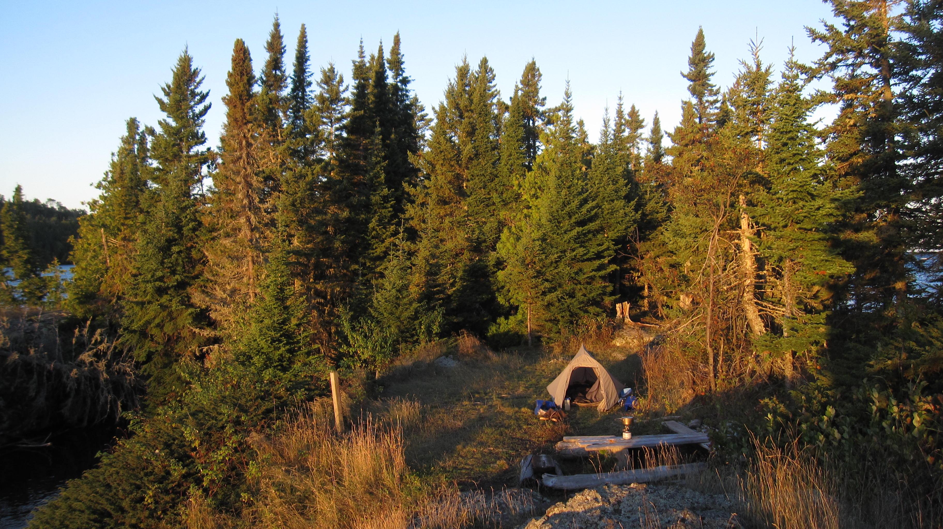 A tent sits on a small peninsula in Lake Superior. Trees rise behind the tent.