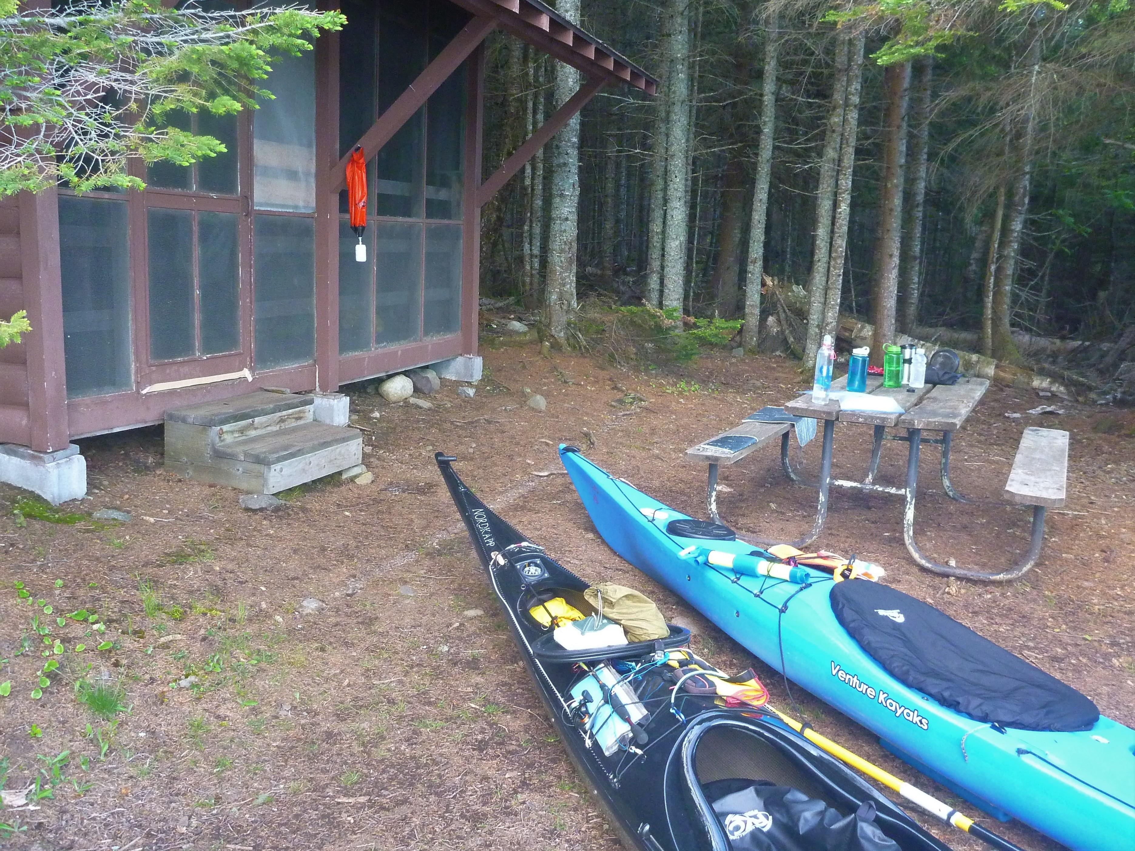 Two kayaks rest in front of a campground shelter.