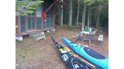 Two kayaks rest in front of a campground shelter.