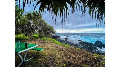 A green picnic table sits in a grassy campsite with the rocky ocean shoreline in the background.