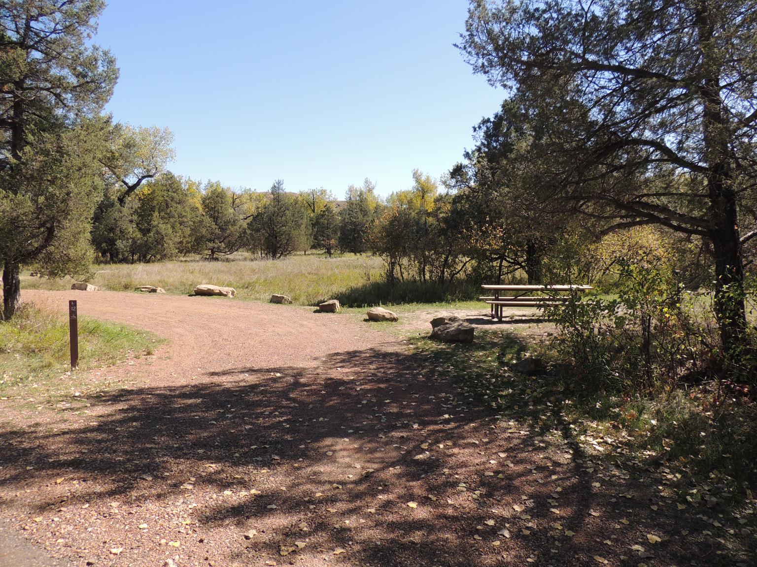 A curved gravel parking pad lined with boulders and an adjacent campsite and picnic table.