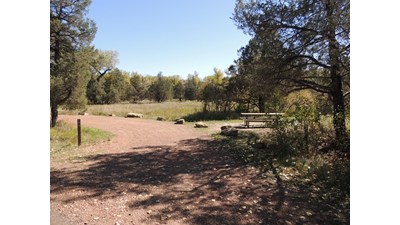 A curved gravel parking pad lined with boulders and an adjacent campsite and picnic table.