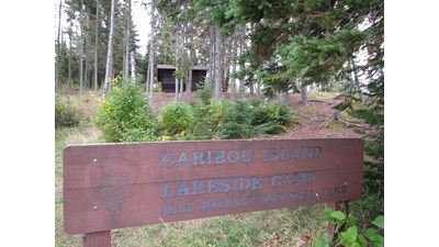 Caribou Island sign with shelter in the distance behind trees.