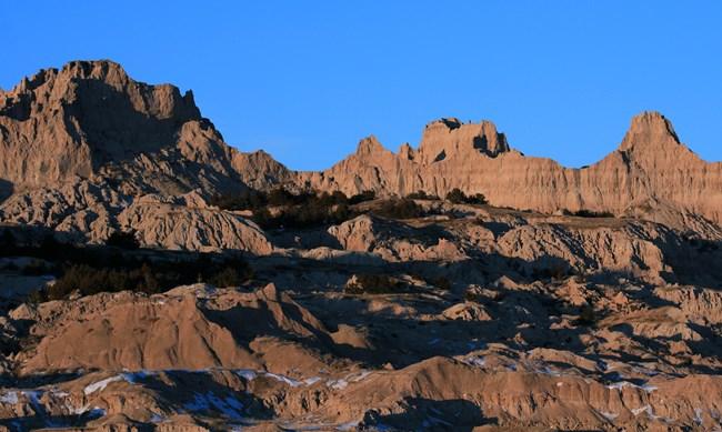 dark plants take root in a large pile of debris crumbling down the side of a jagged badlands butte.