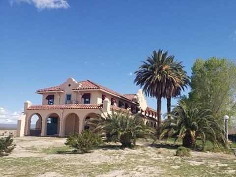 A tan building on the left, with palm trees and a green lawn in the foreground and right side.