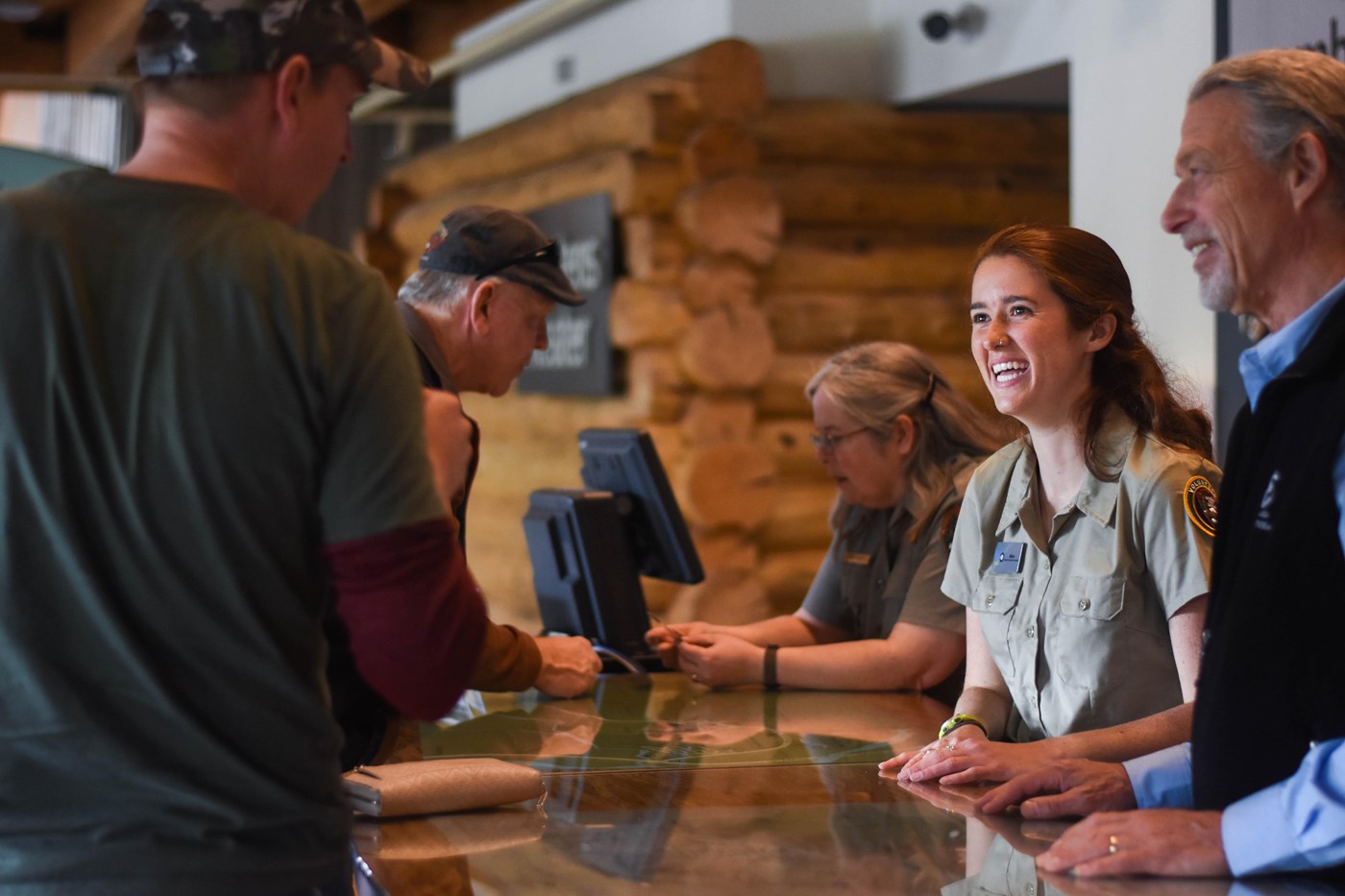 a volunteer and park ranger speak to people at a desk
