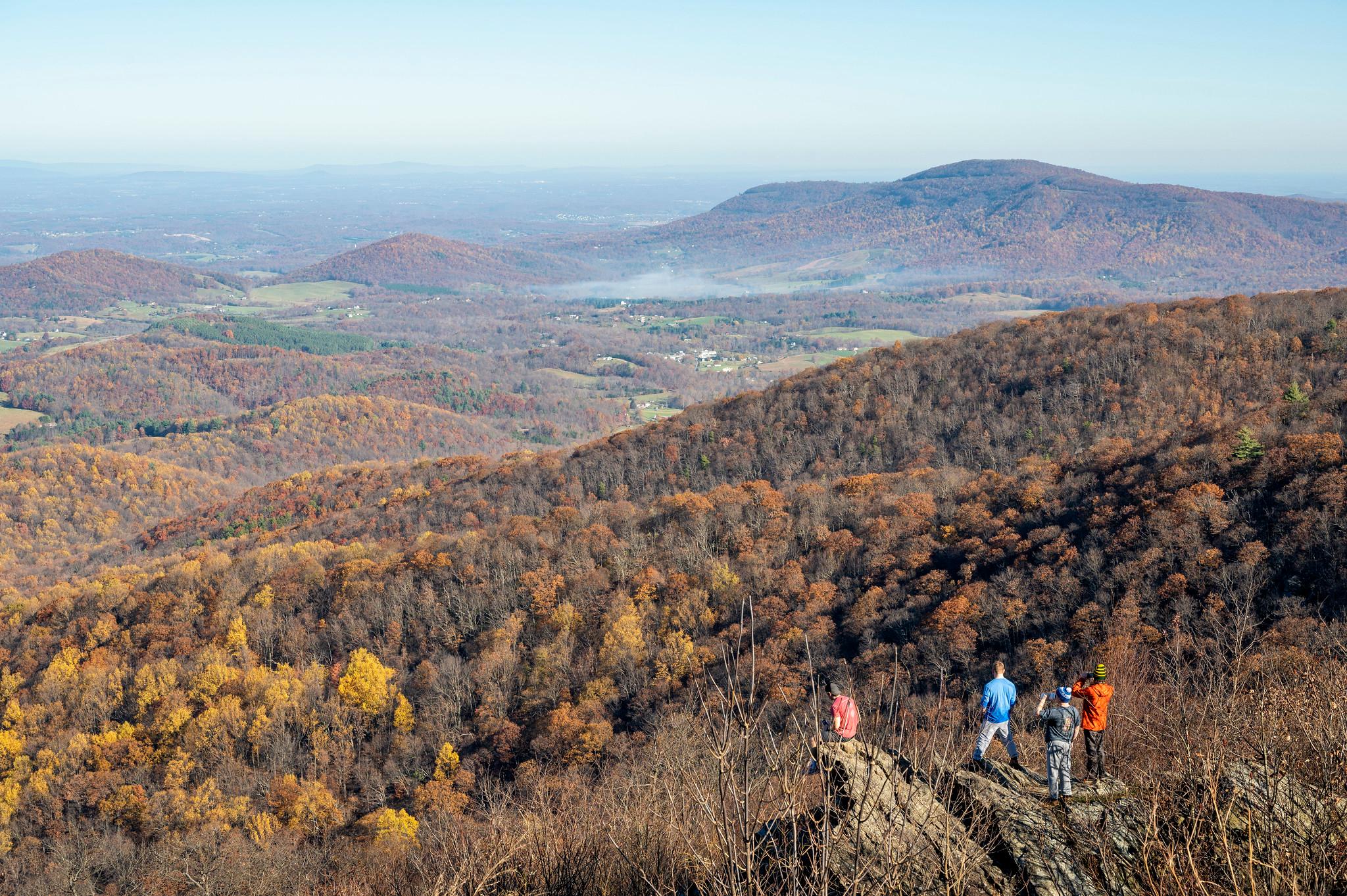 Visitors stand on a rocky outcrop overlooking the receding mountains.