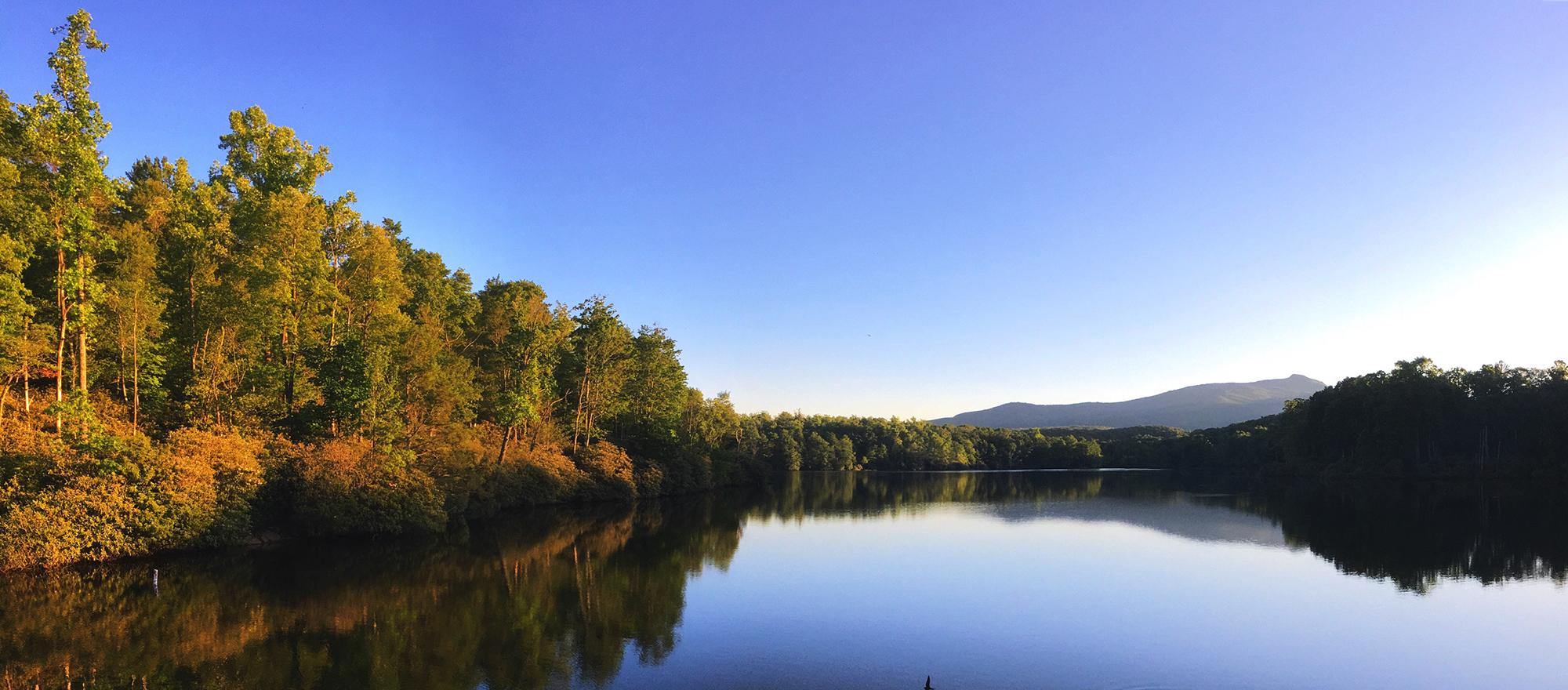 Still waters of a lake reflect a deep blue sky and the fall colors of the trees surrounding it.