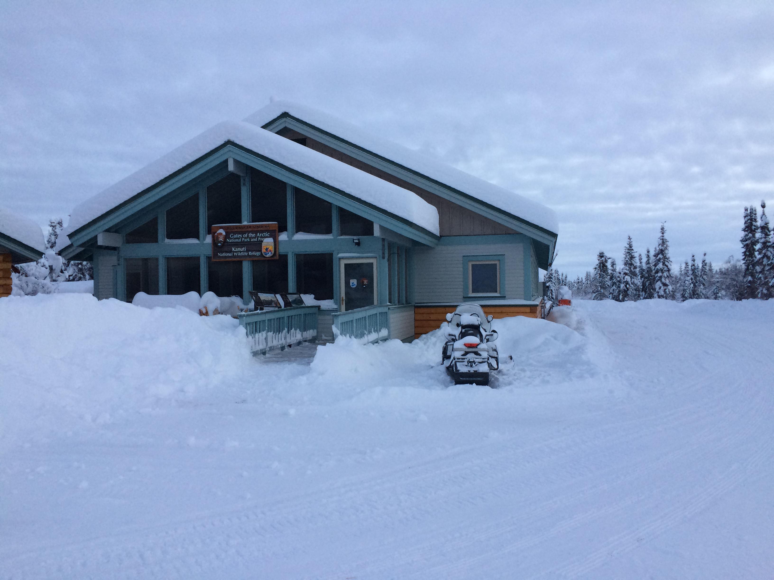 View of blue wooden A-frame building in the snow with a snowmobile in front