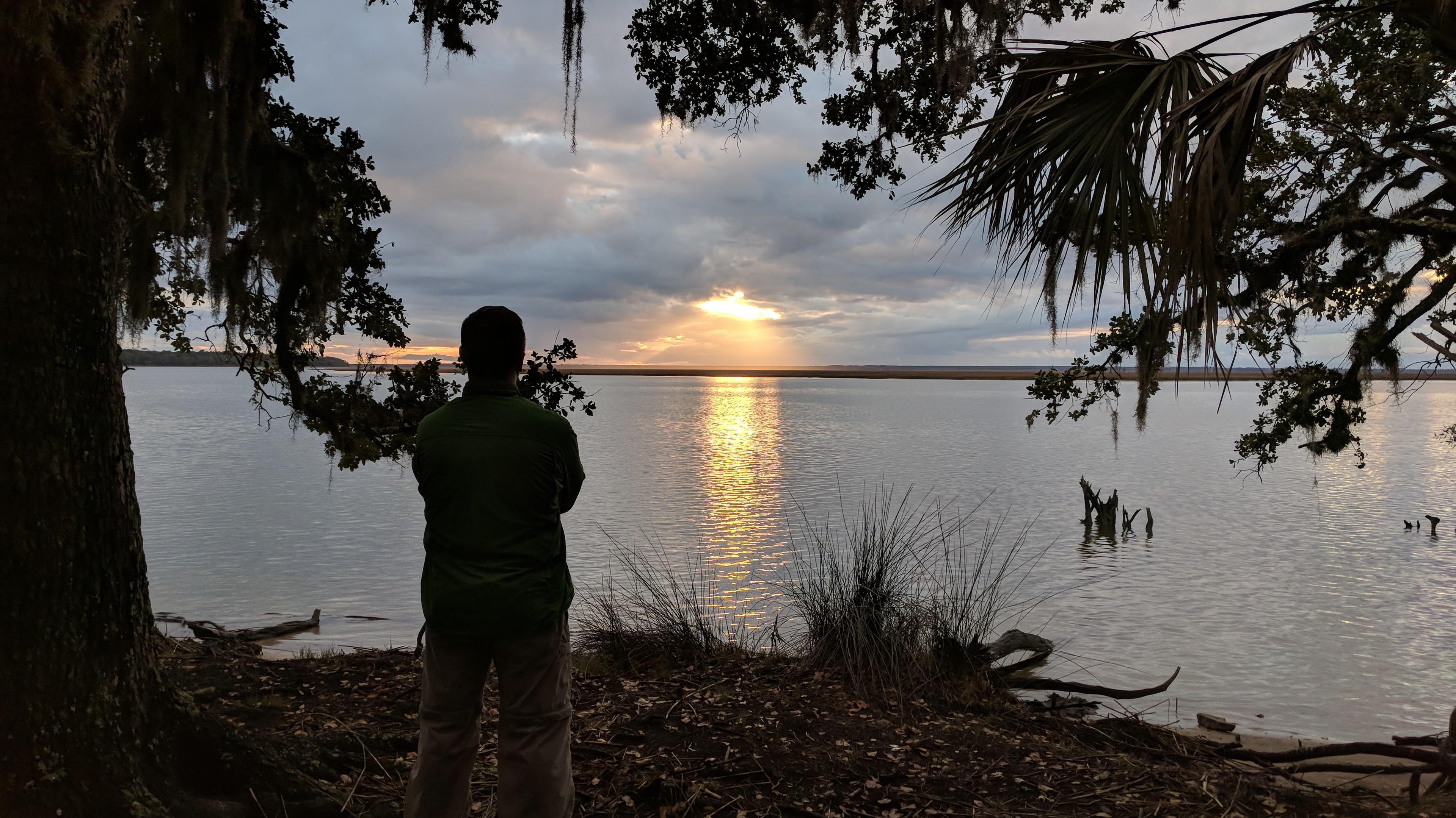 camper watches sunset across water from camp