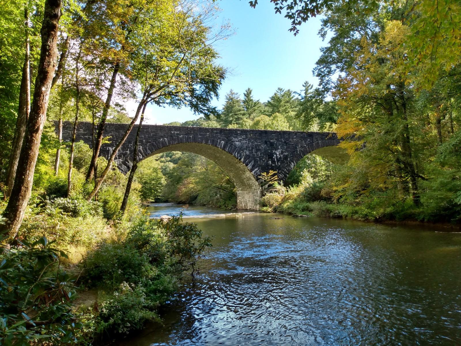 A stone bridge arches over a forested river