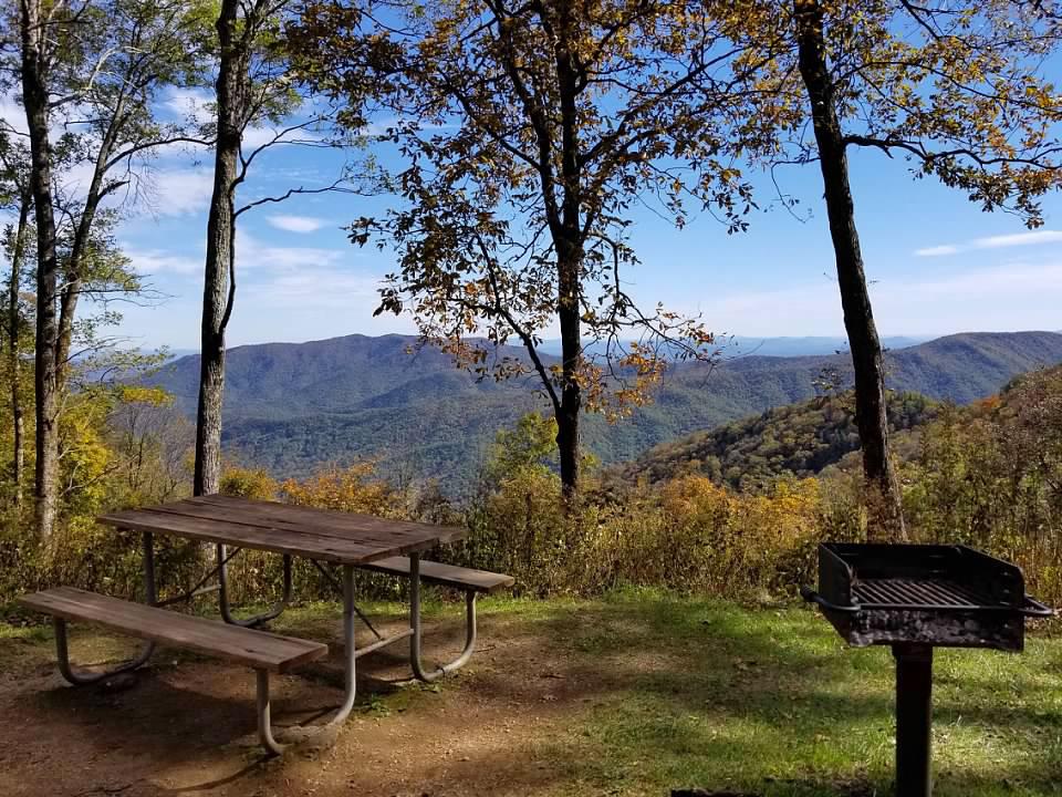 A picnic table sits at the edge of an opening in the forest, with mountains in the distance
