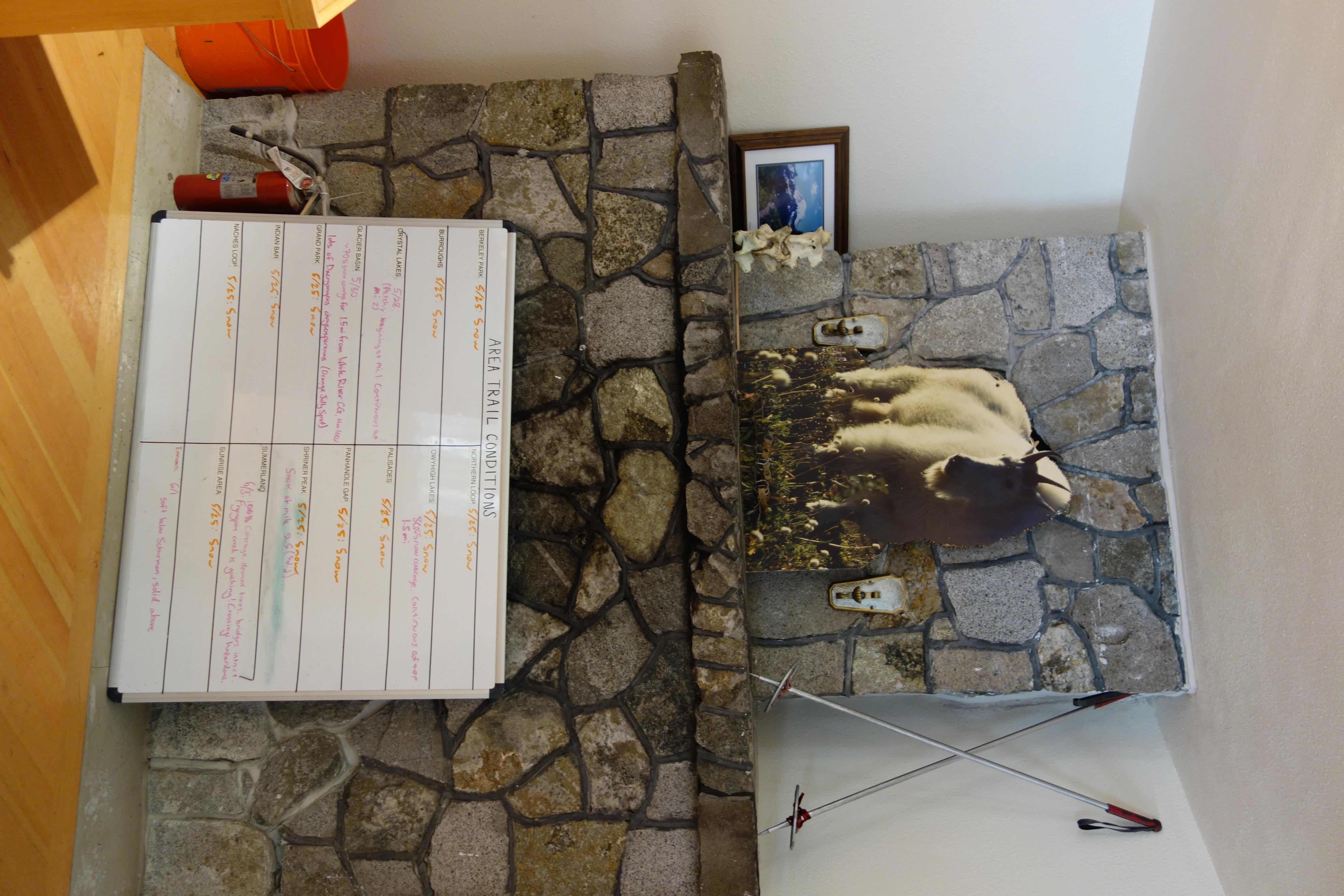 A "trail conditions" white board leans against a rock fireplace with a cut out of a mountain goat.