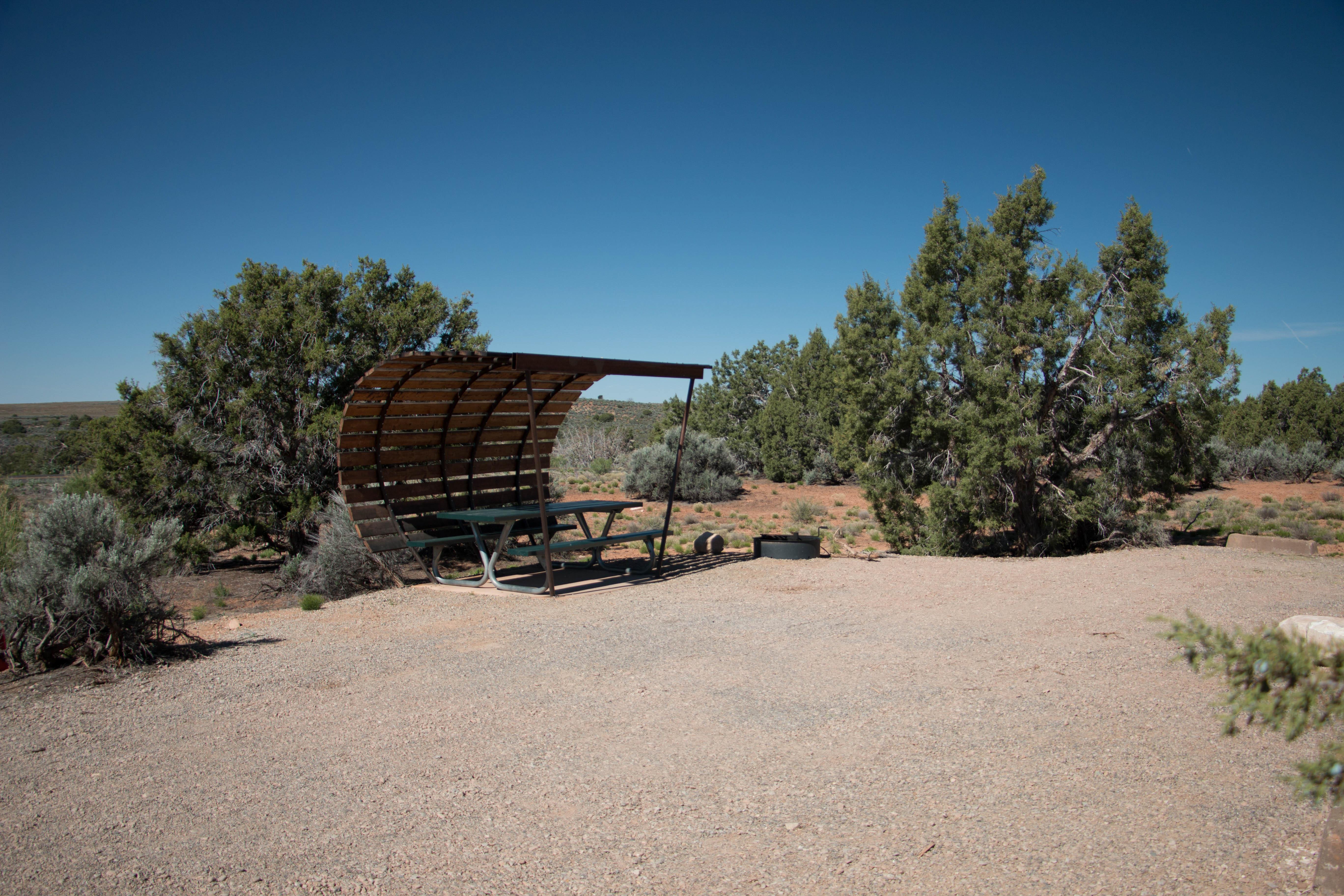 a gravel area with a picnic table under a shade structure
