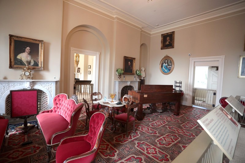 Arlington House Interior Portraits hang on the walls of the parlor room with red velvet furniture and a small dining table.