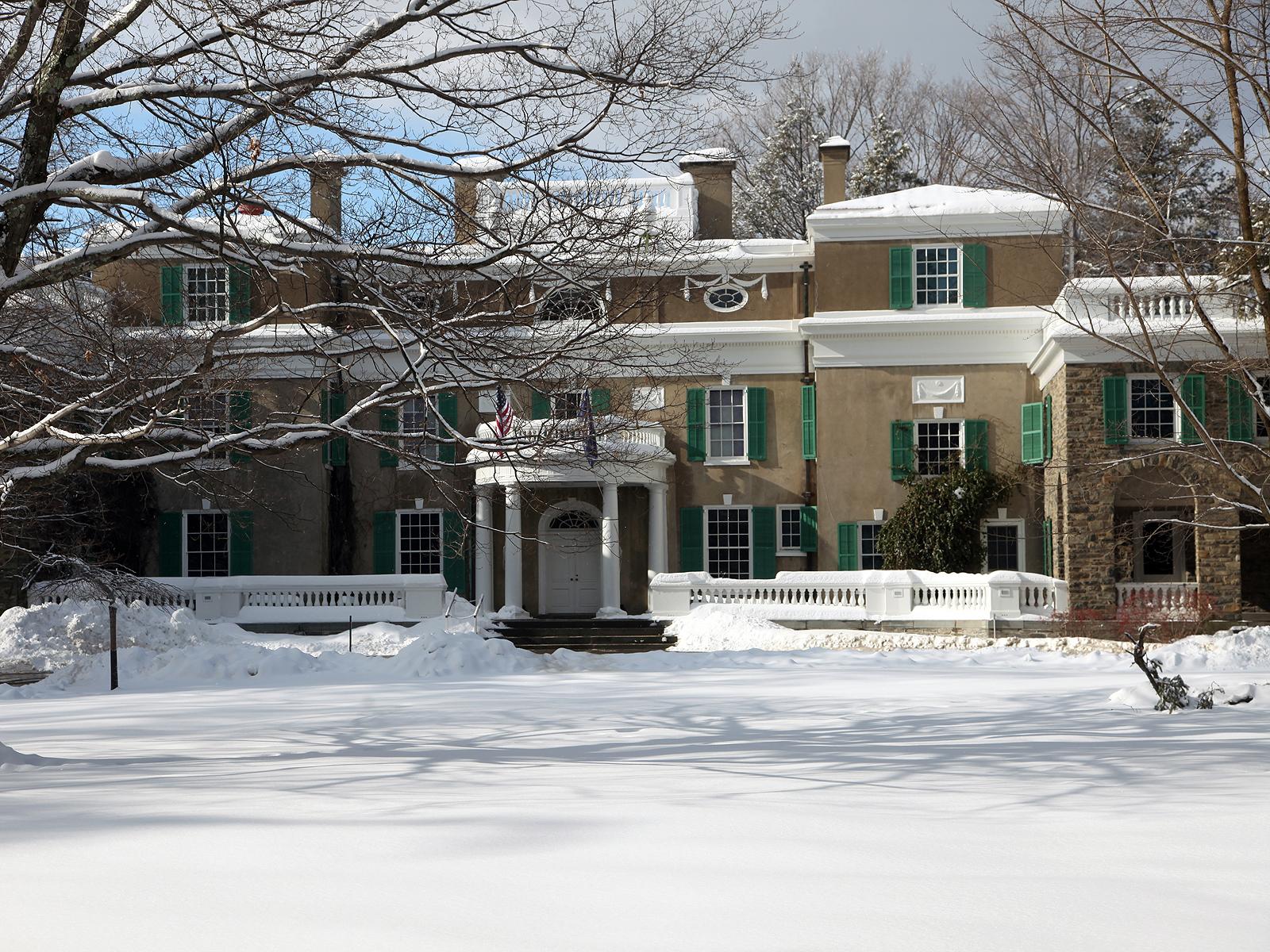 A stucco house with wood portico surrounded by a snowy lawn.