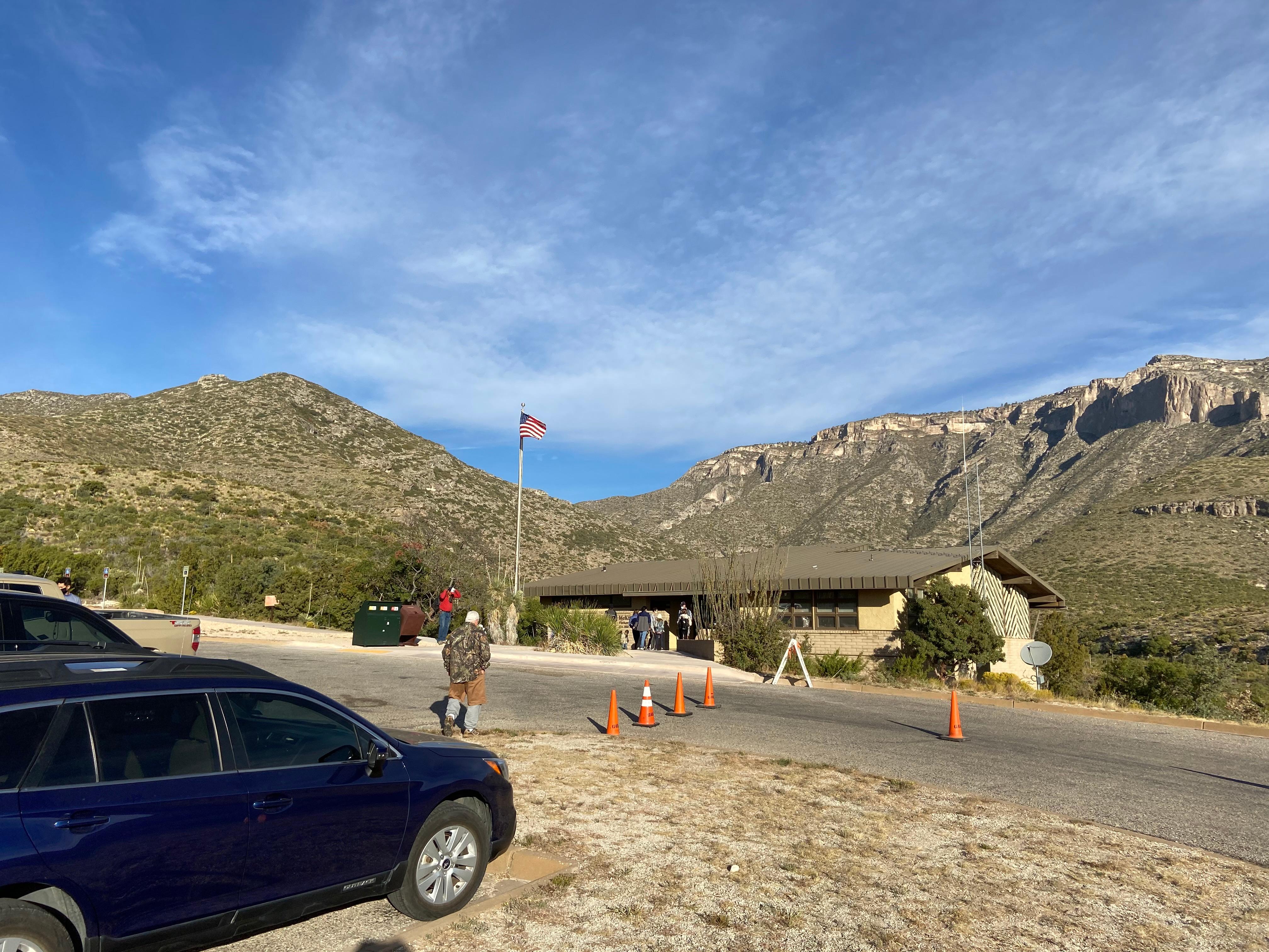 The flag flies in front of s yellow and brown building at the mouth of a wide canyon