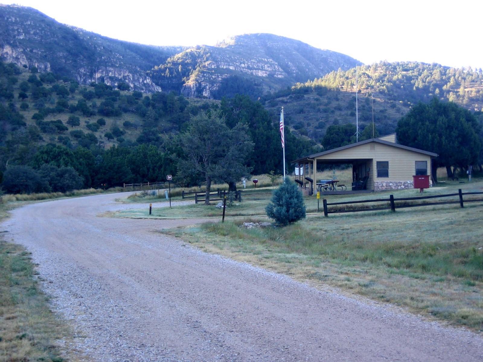 A road passes by the front of a small building with a flag pole in front of it.