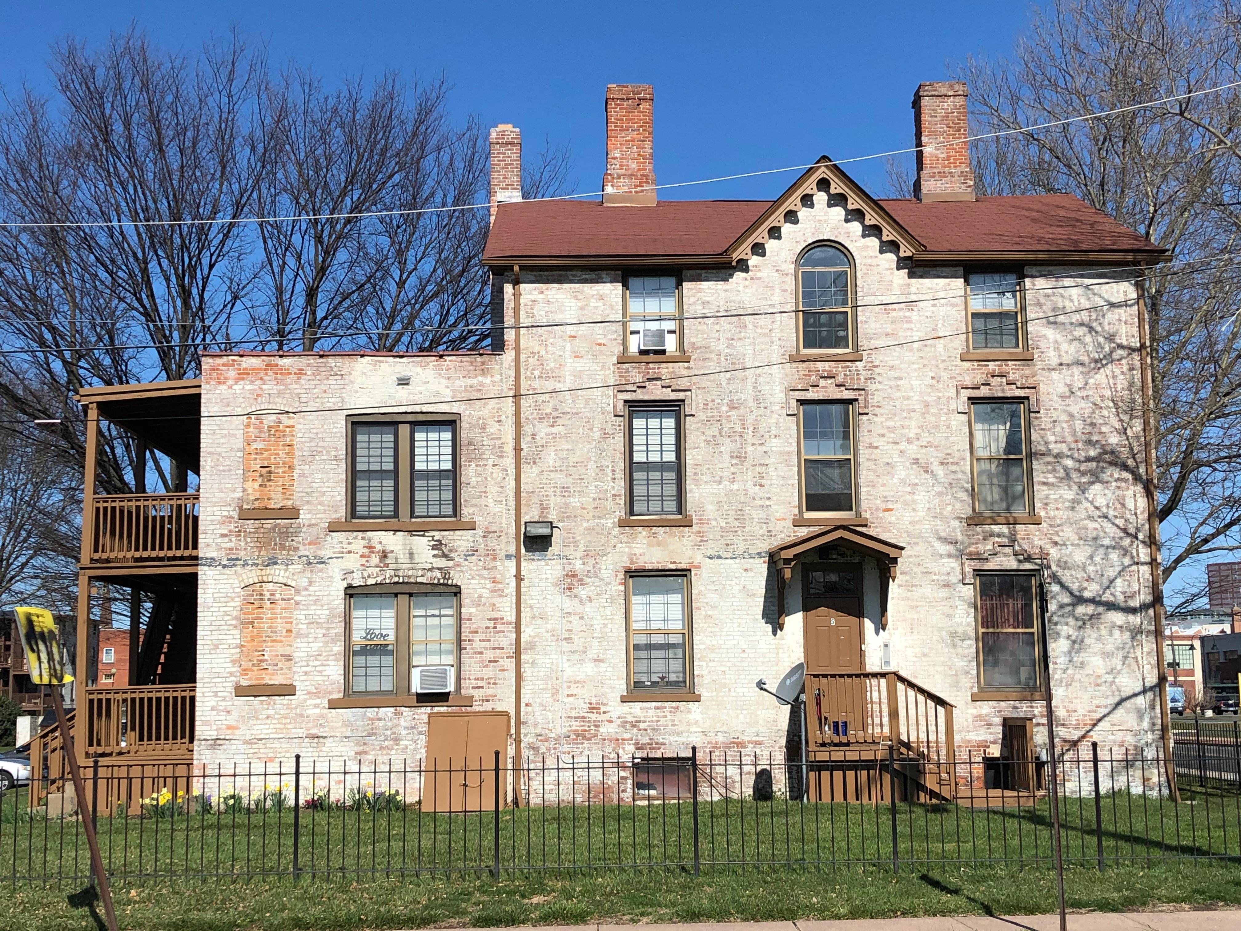 A white stone building with multiple windows and three chimneys with green grass and a black fence.