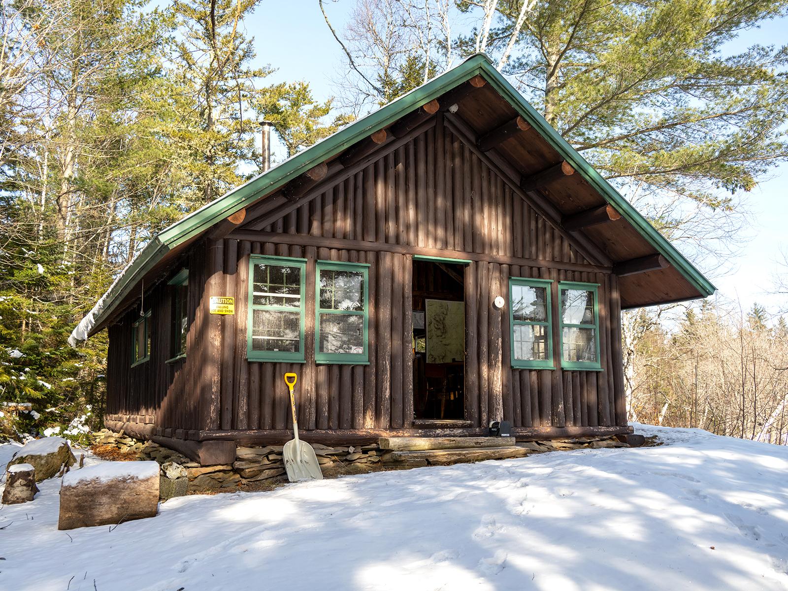 A log cabin on a snowy hill. Evergreen trees frame the back for the cabin.