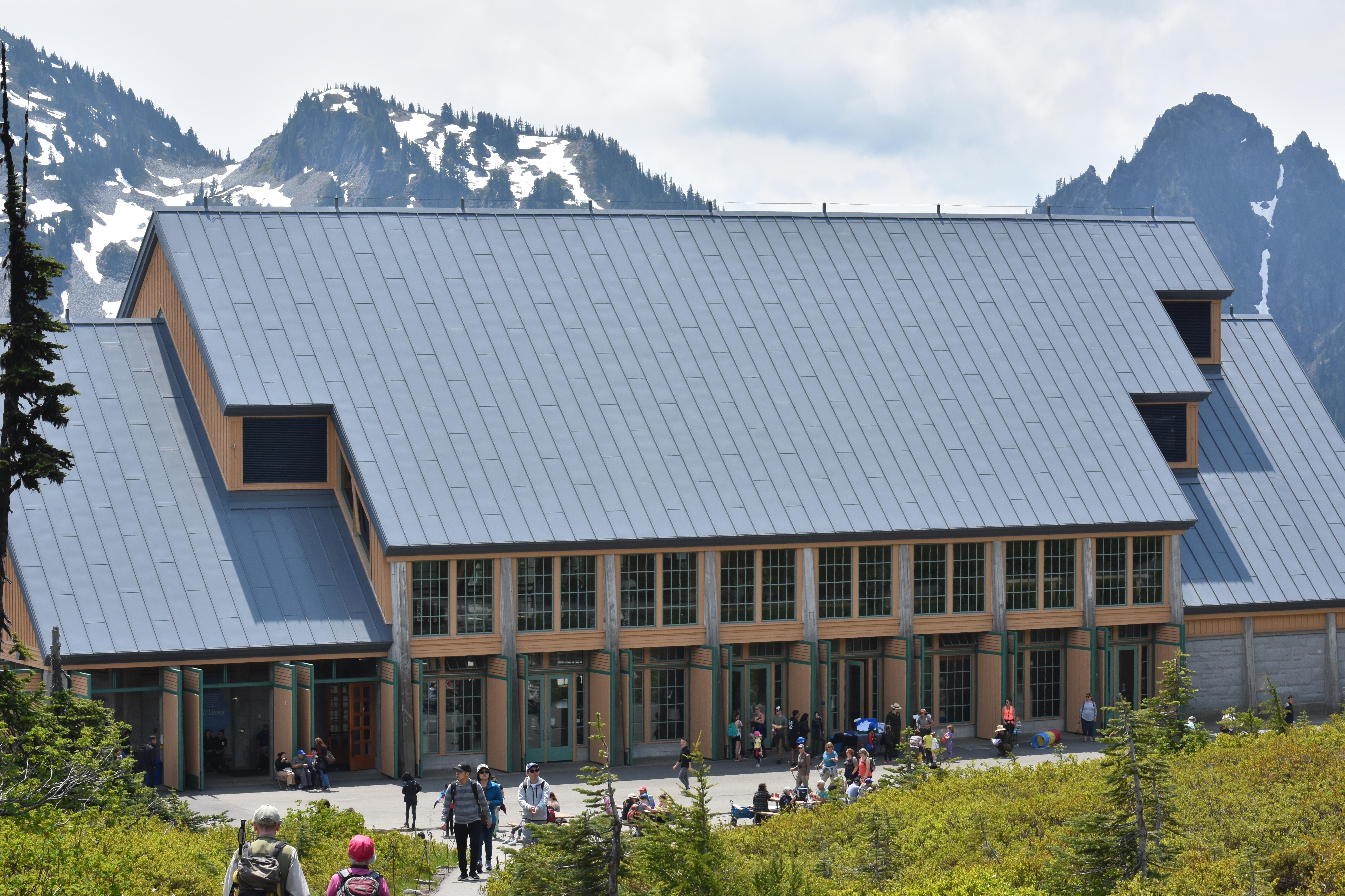 A large building with a great roof and lots of windows sits near a trailhead with lots of people.