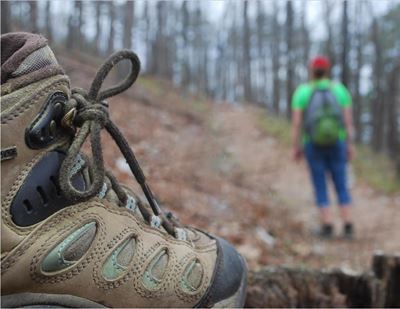 Close up of a hiking boot on the trail a hiker in the distance
