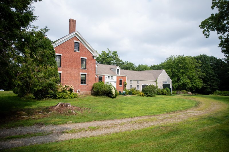 Approach to the Frances Perkins Homestead A sandy brown driveway curves through green grass towards the two story-red brick homestead and grey