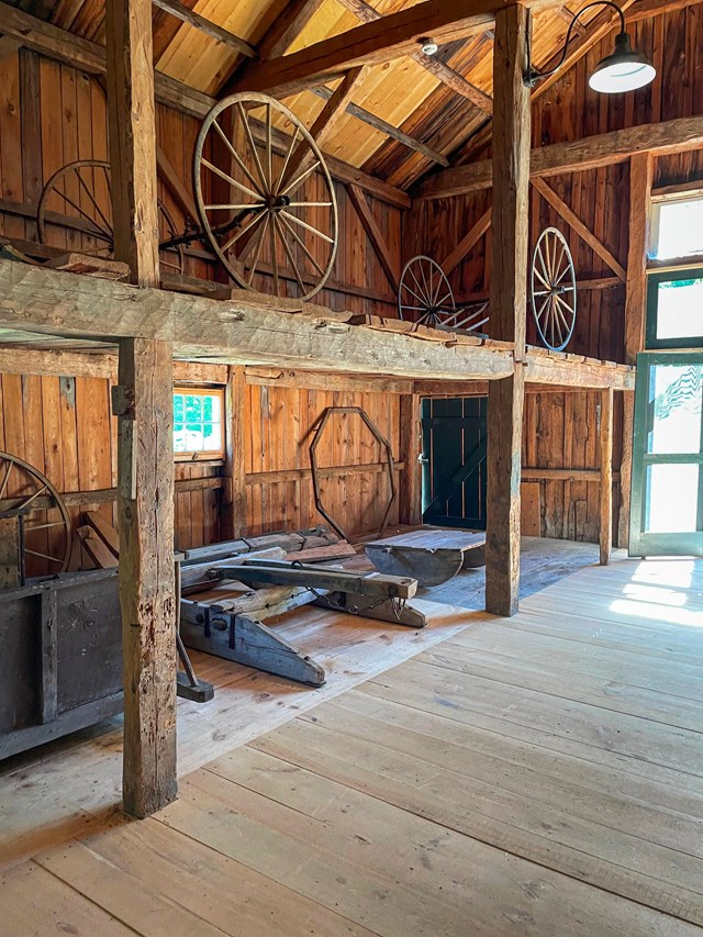 The sun shines upon wooden wagon wheels and other antique farm implements lining the rustic hewn wal