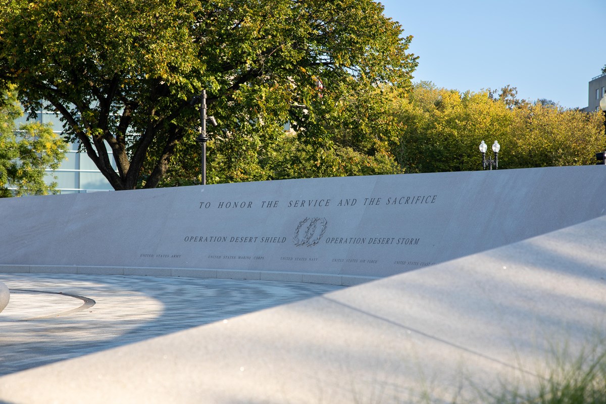 A curving wall in front of some trees.