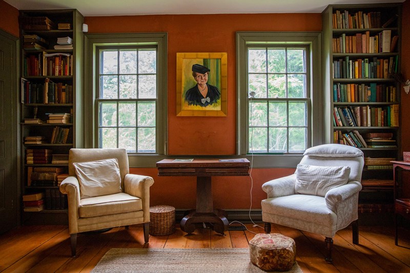 Inside the Perkins Homestead Two white sofa chairs stand in front of two windows in a room with red walls and a portait of Perkin