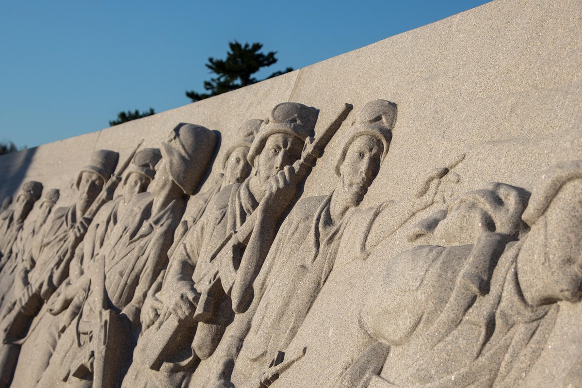 Bas relief sculpture of infantrymen carrying rifles and moving to the right.