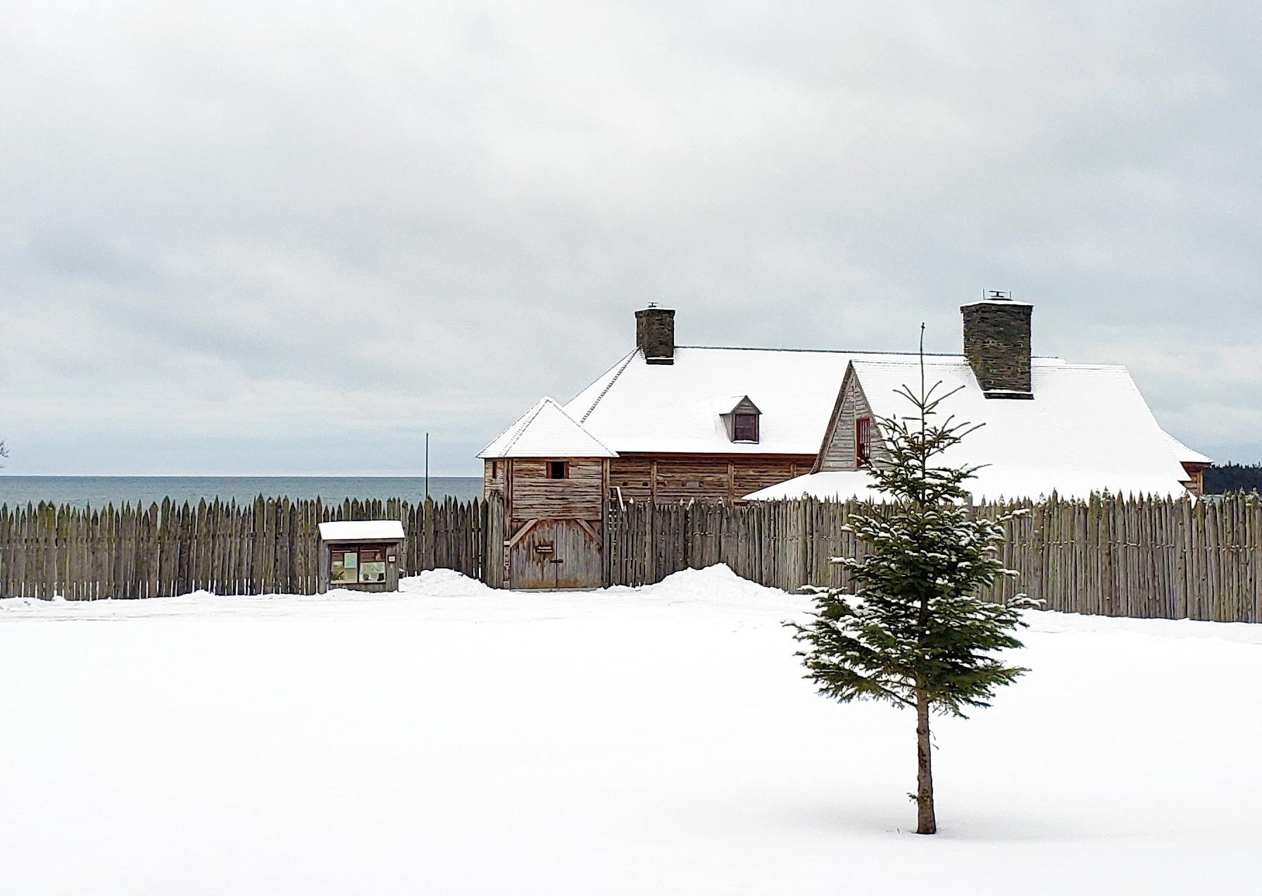 Historic wooden buildings behind a palisade in a snowy landscape.