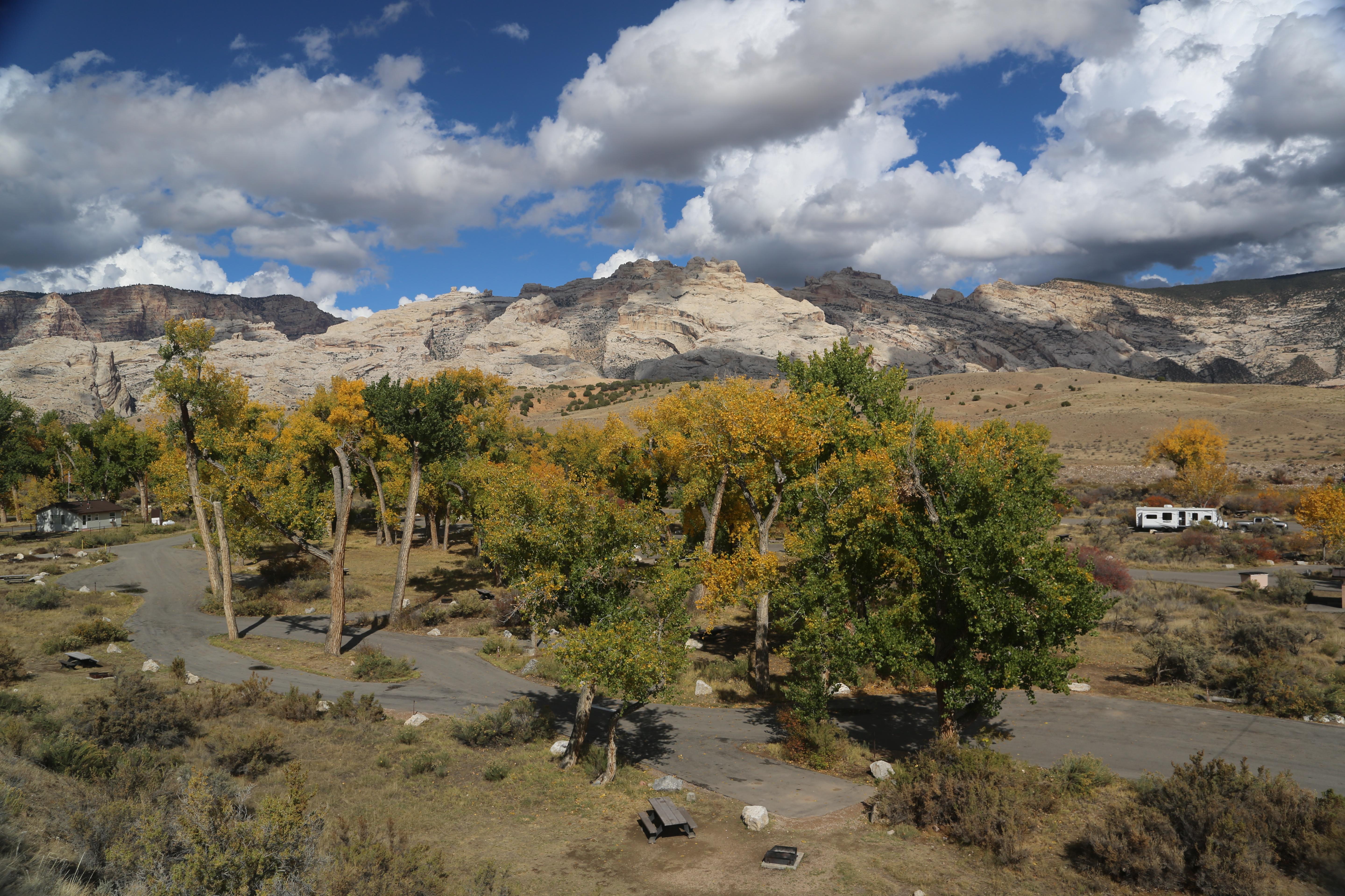Trees with yellow leaves stand above campsites with a rocky mountain in the background.