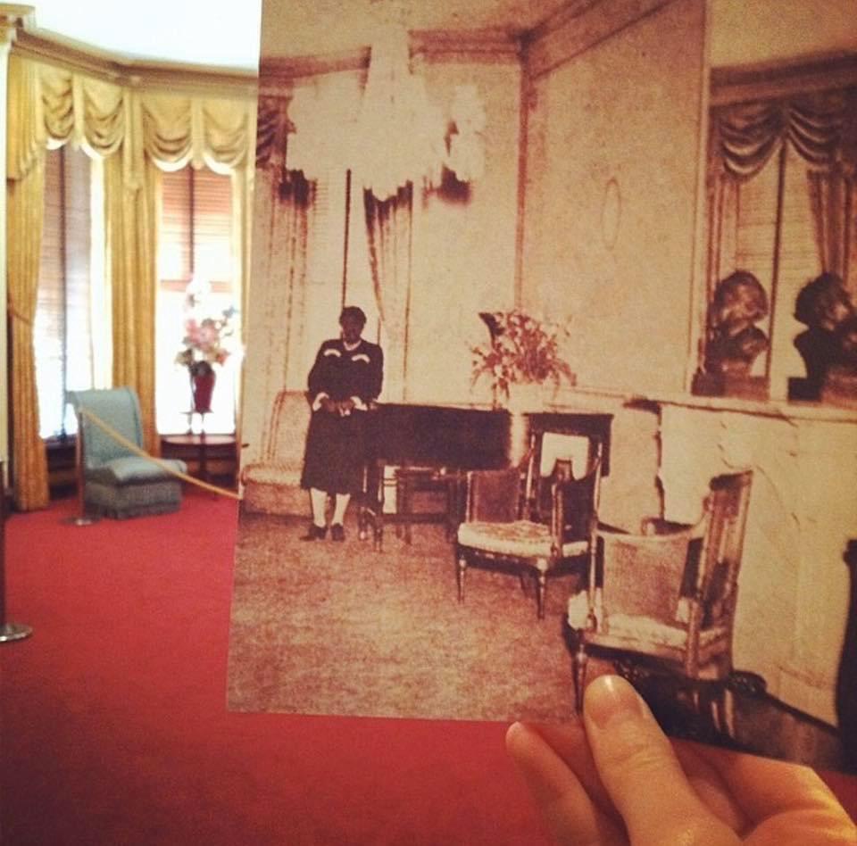 A historic photo of the parlor room is held up in front of the same view today.