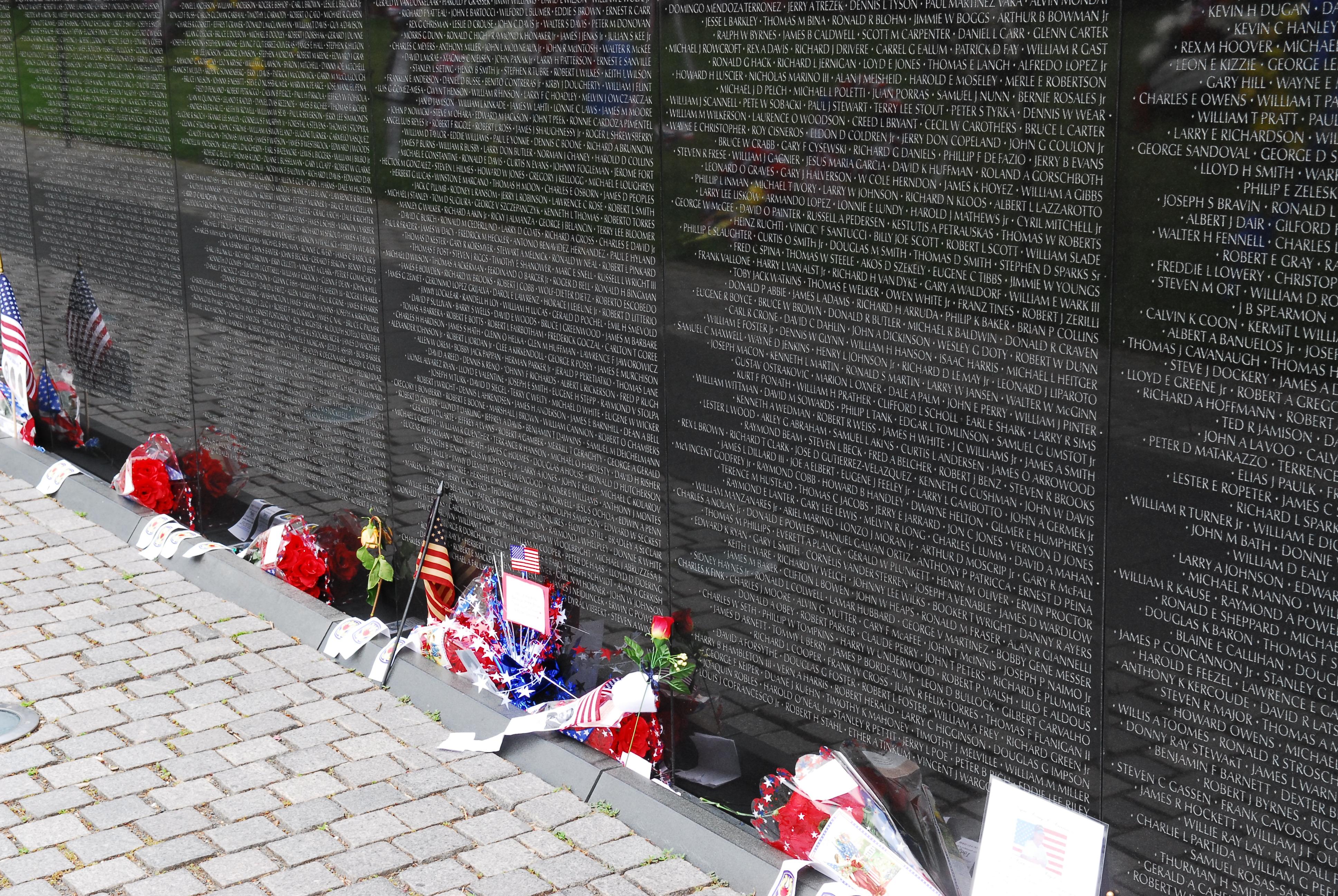 Notes and flags set at the base of the Vietnam Veterans Memorial, a black wall inscribed with names.