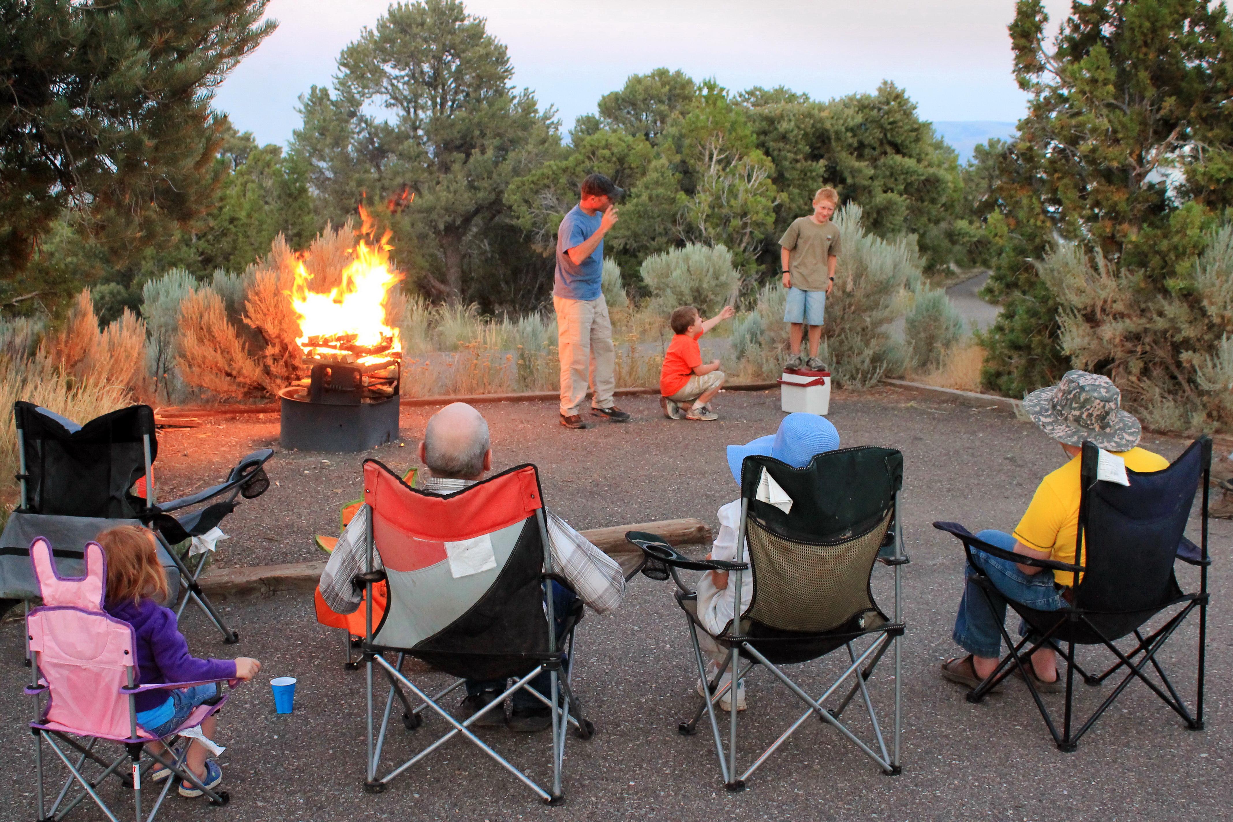 A family is gathered around a blazing campfire in the evening.
