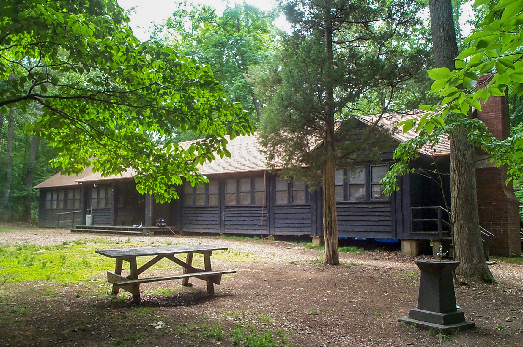 A large brown wooden building is surrounded by tree. A picnic table sits on the lawn in front of it