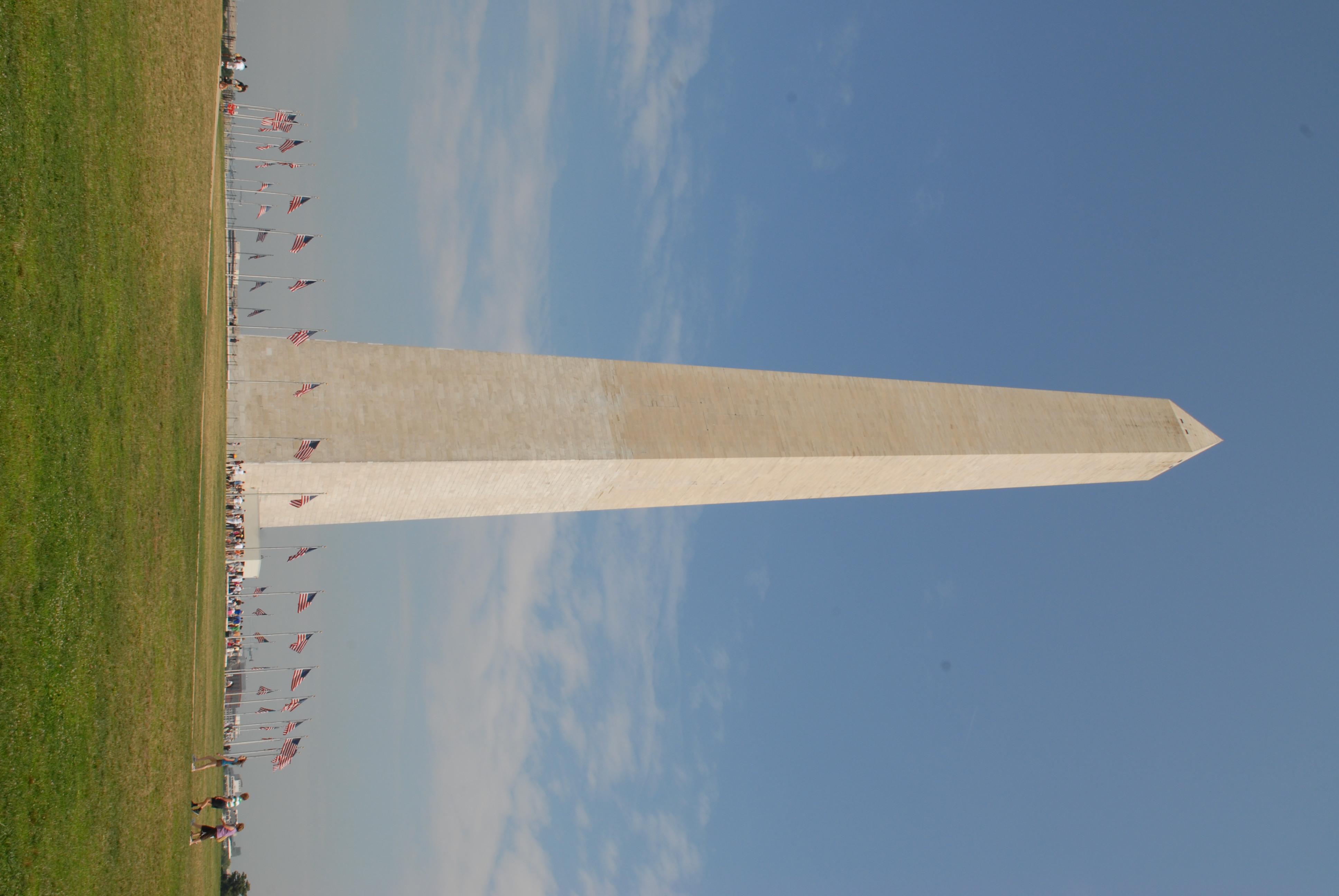 The Washington Monument, a white marble obelisk, towers above a ring of US Flags.