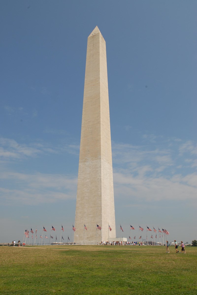 The Washington Monument, a white marble obelisk, towers above a ring of US Flags.