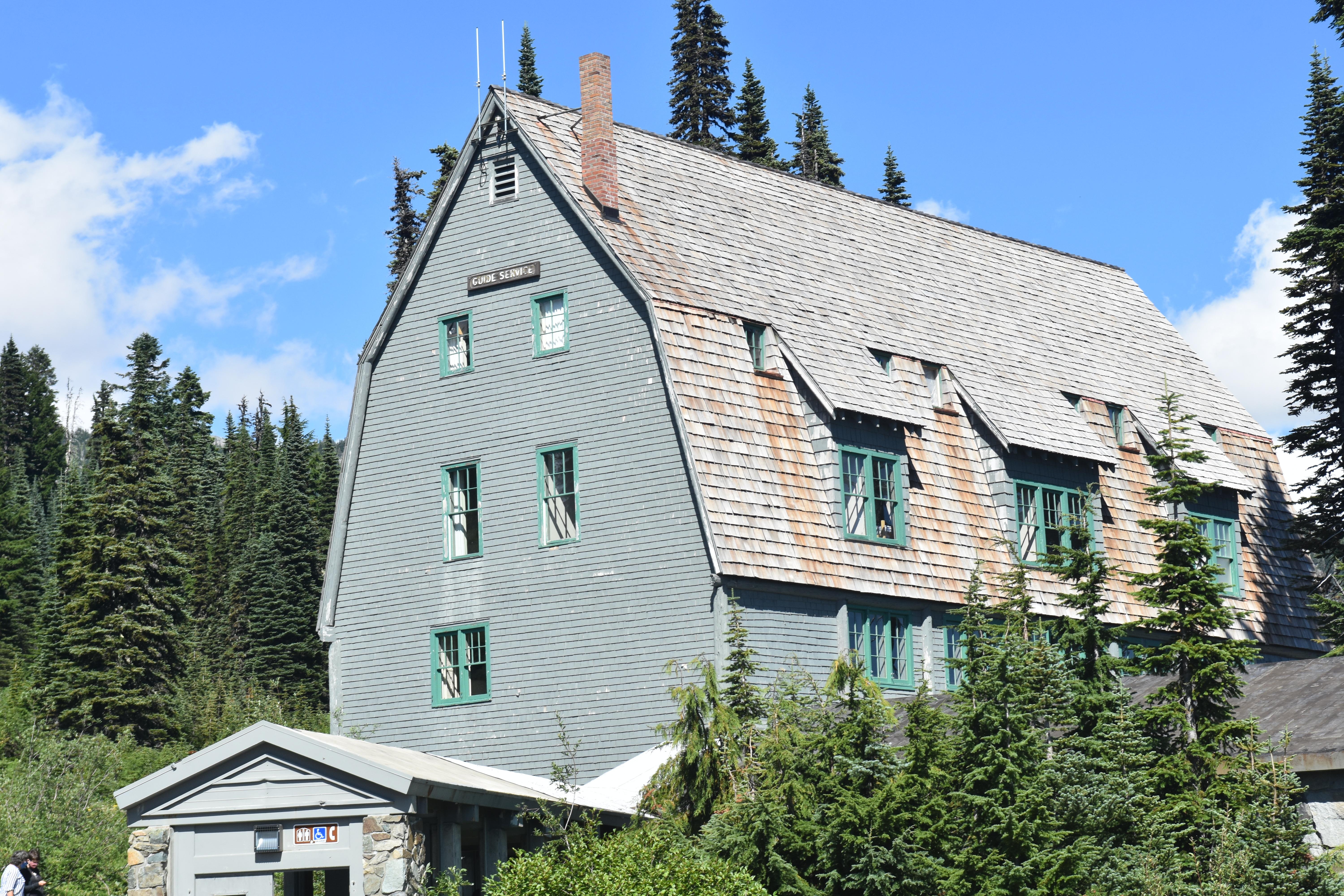 A grey steeply-angled building sits surrounded by green trees.