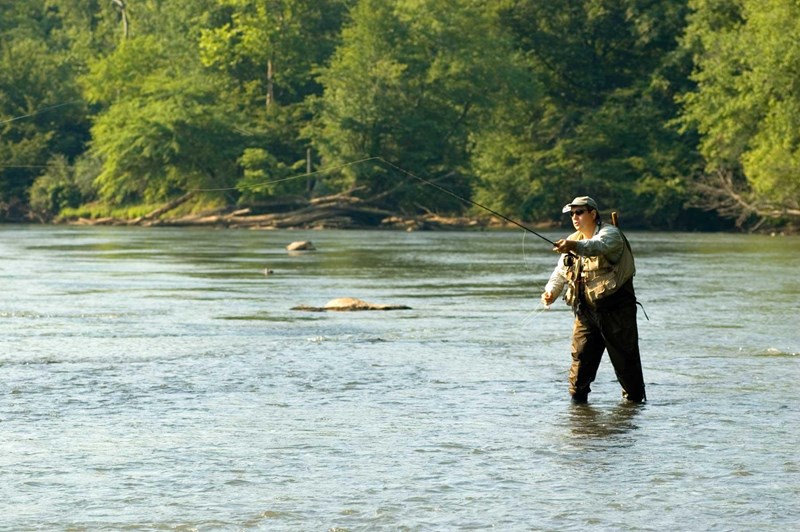 Fishing Angler in waders holding a fishing rod in the middle of a shallow river