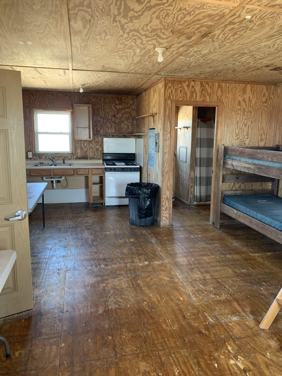 Rustic cabin interior showing bunk beds, kitchenette and doorway to restroom