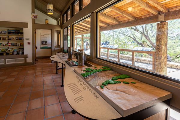 A view from inside the visitor center through large windows, looking out to a covered patio.