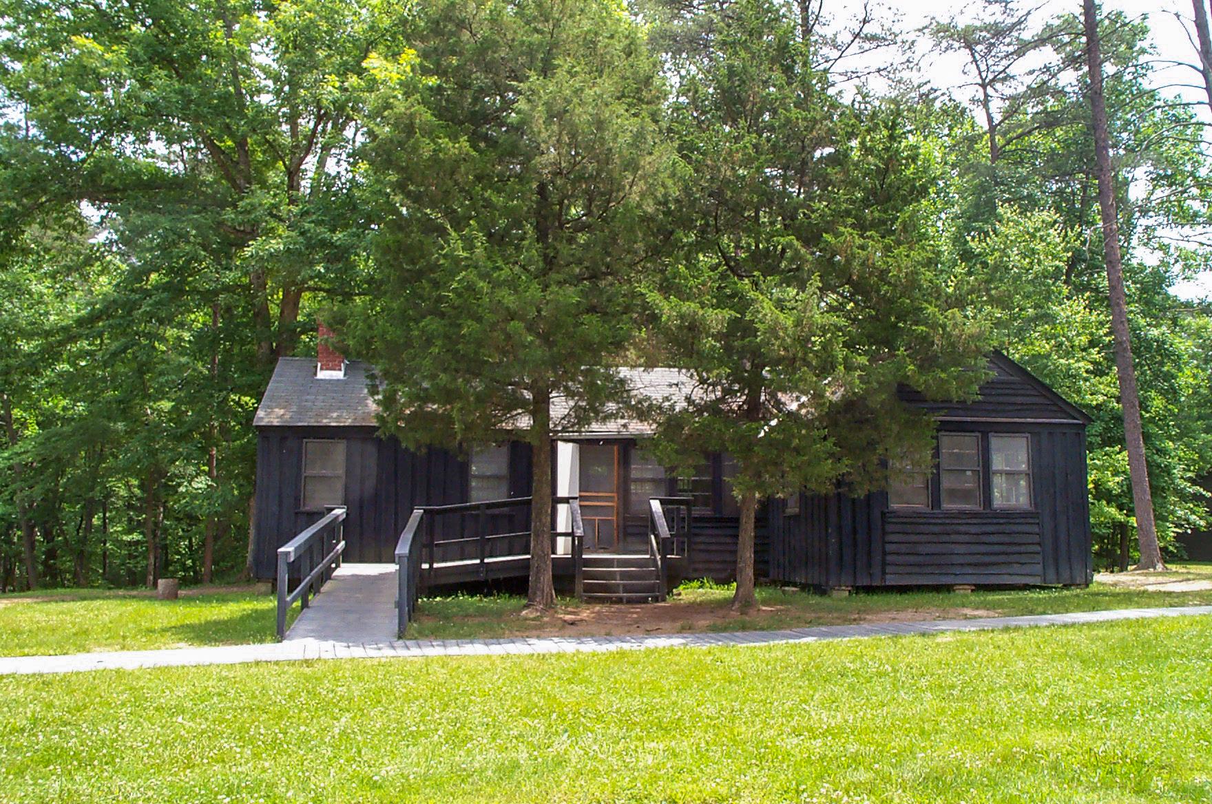 A dark brown wooden building with a ramp stands among trees with a grassy lawn