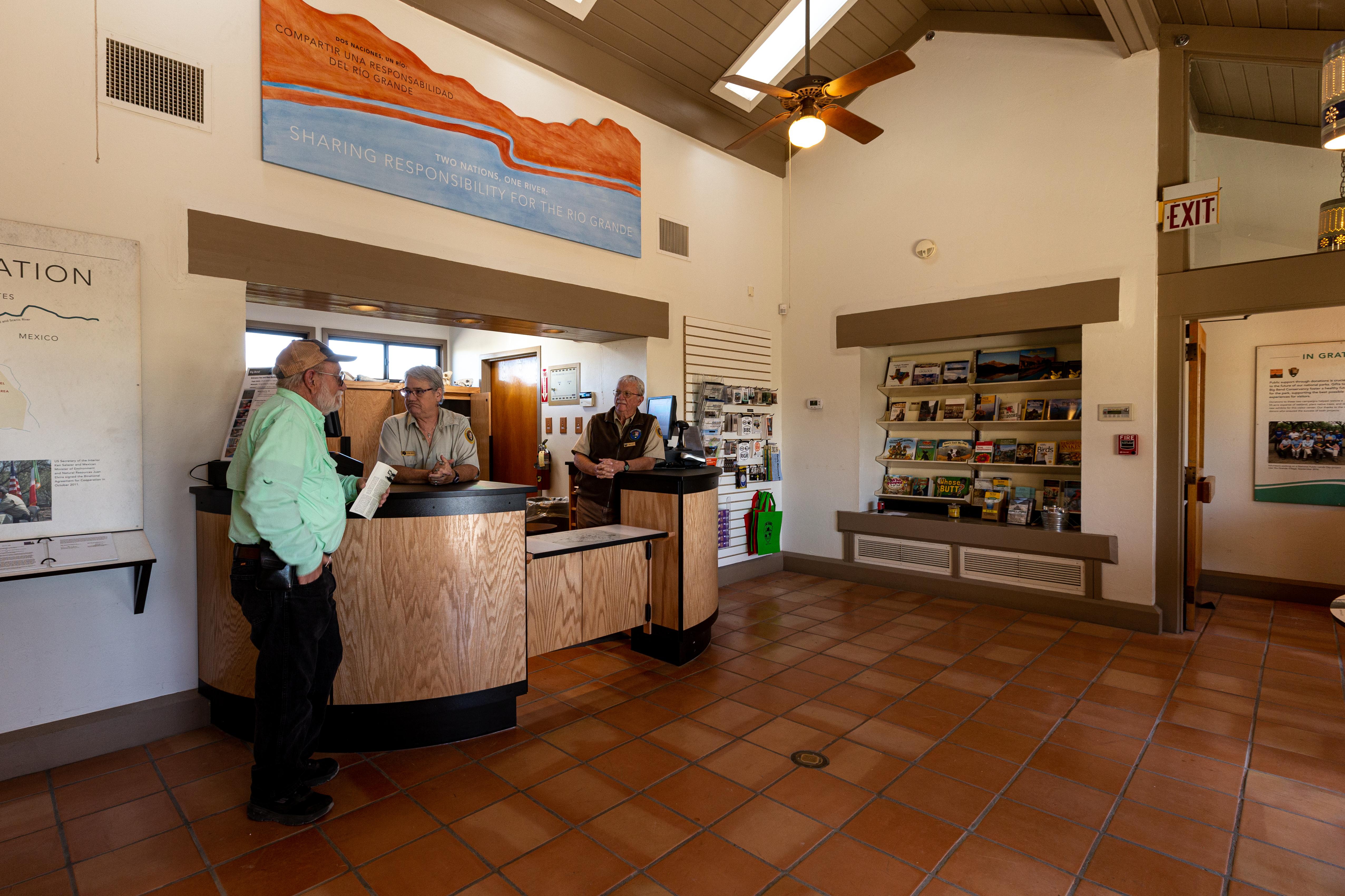 Three people stand inside a room with a high ceiling and tile floors.