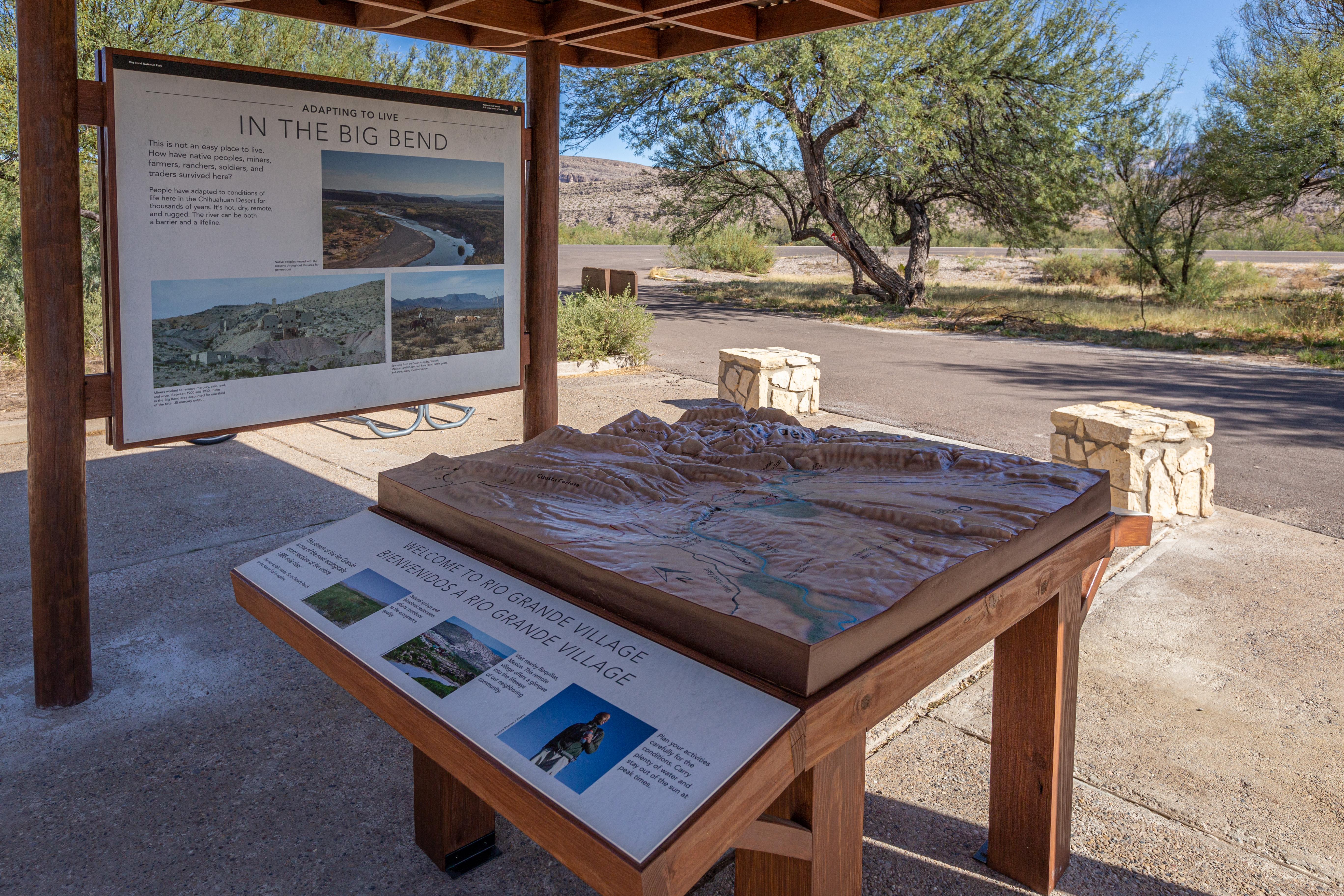 A relief map and information panels sit under a shade structure.