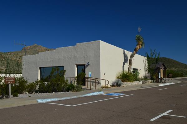 A side view of a white-walled adobe building with desert plants out front.