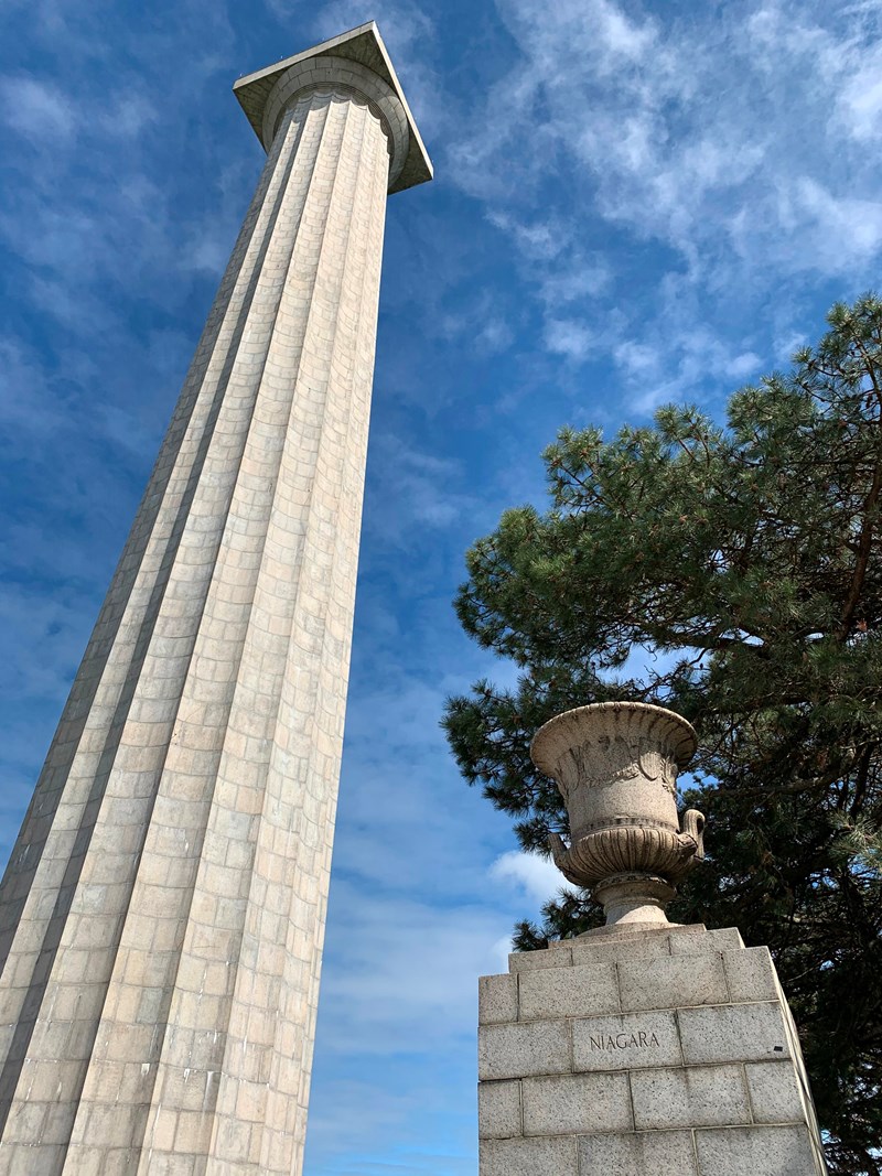 It is tall! 352 foot tall stone memorial column rises up to touch blue sky. In front a 5' urn on pedestal
