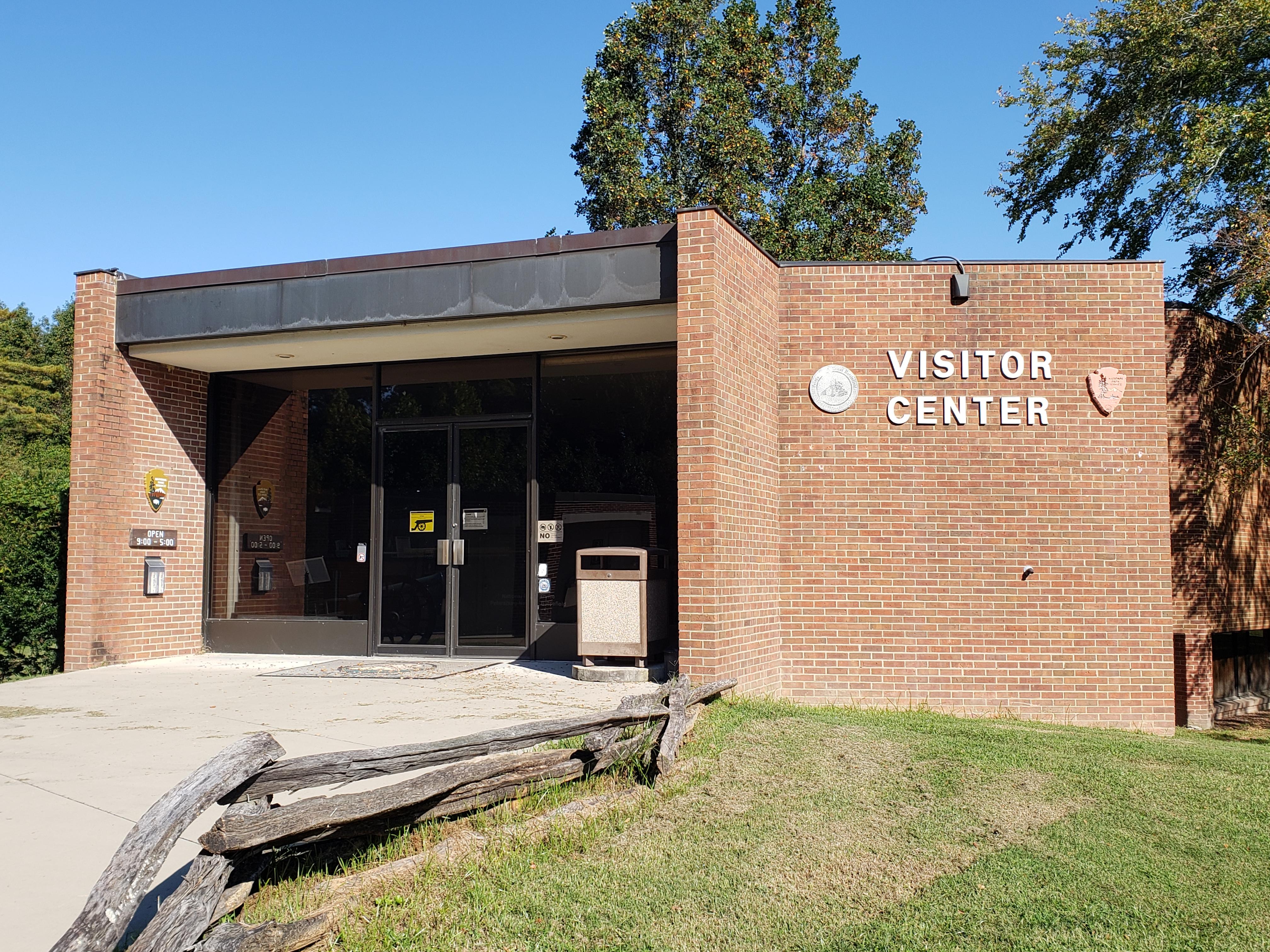Pictured is the front of the brick visitor center under a cloudless blue sky.
