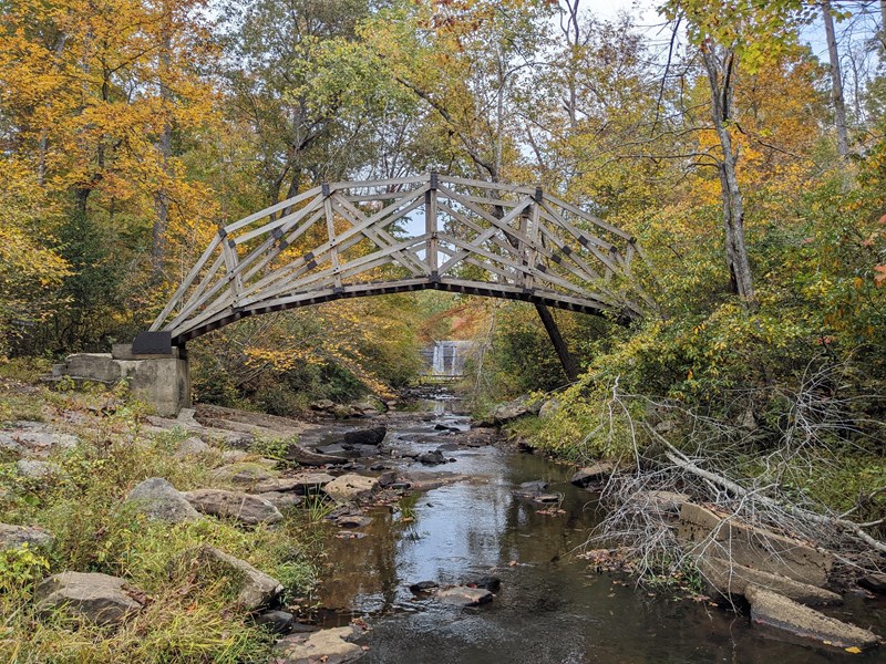 Bridge along the South Valley Trail in Fall An arched wooden bridge above a creek surround by a yellow and orange fall forest